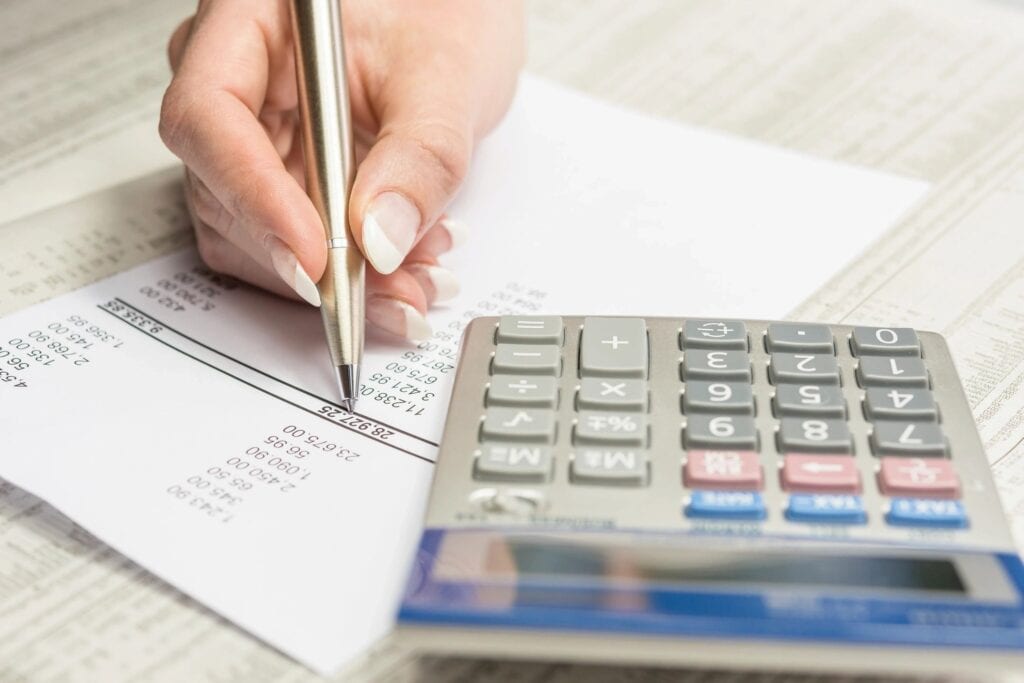 A person writing on paper next to a calculator.