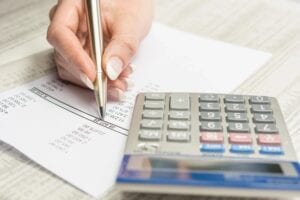 A person writing on paper next to a calculator.
